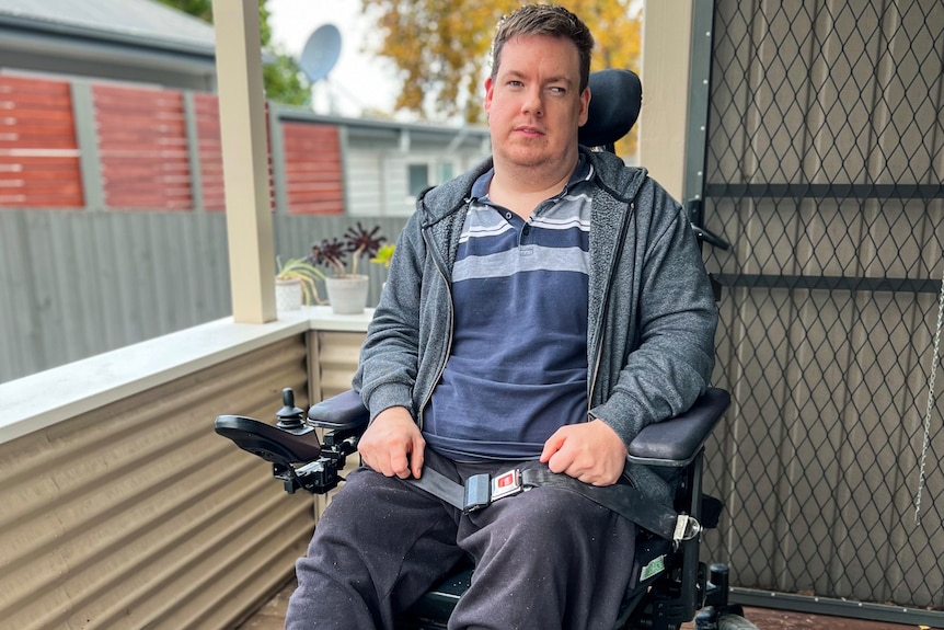 A man in a blue jumper sitting outside in a wheelchair
