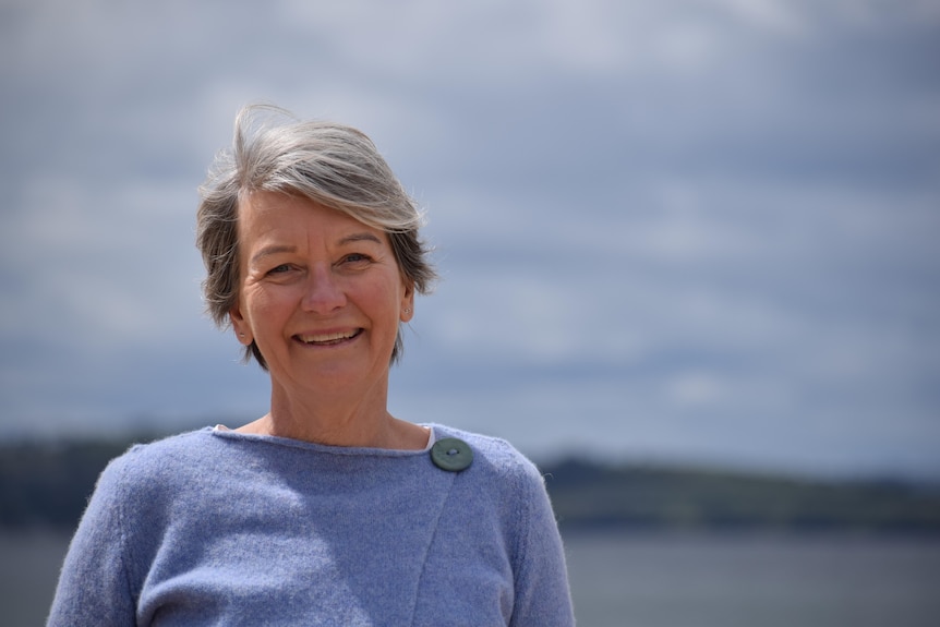 A woman with grey hair and a blue/purple jumper smiling at the camera.