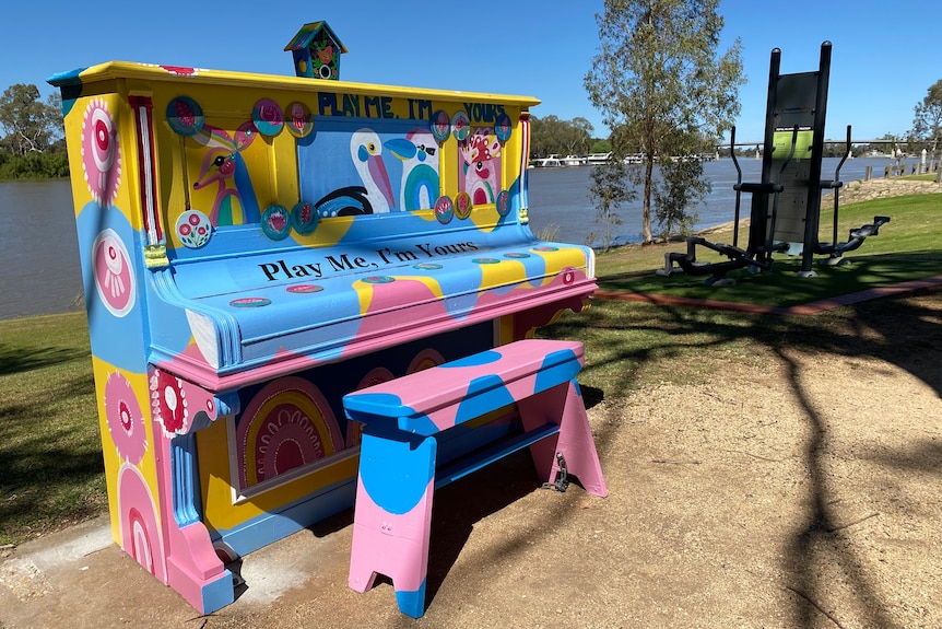 A brightly coloured piano, placed outside along a river. 