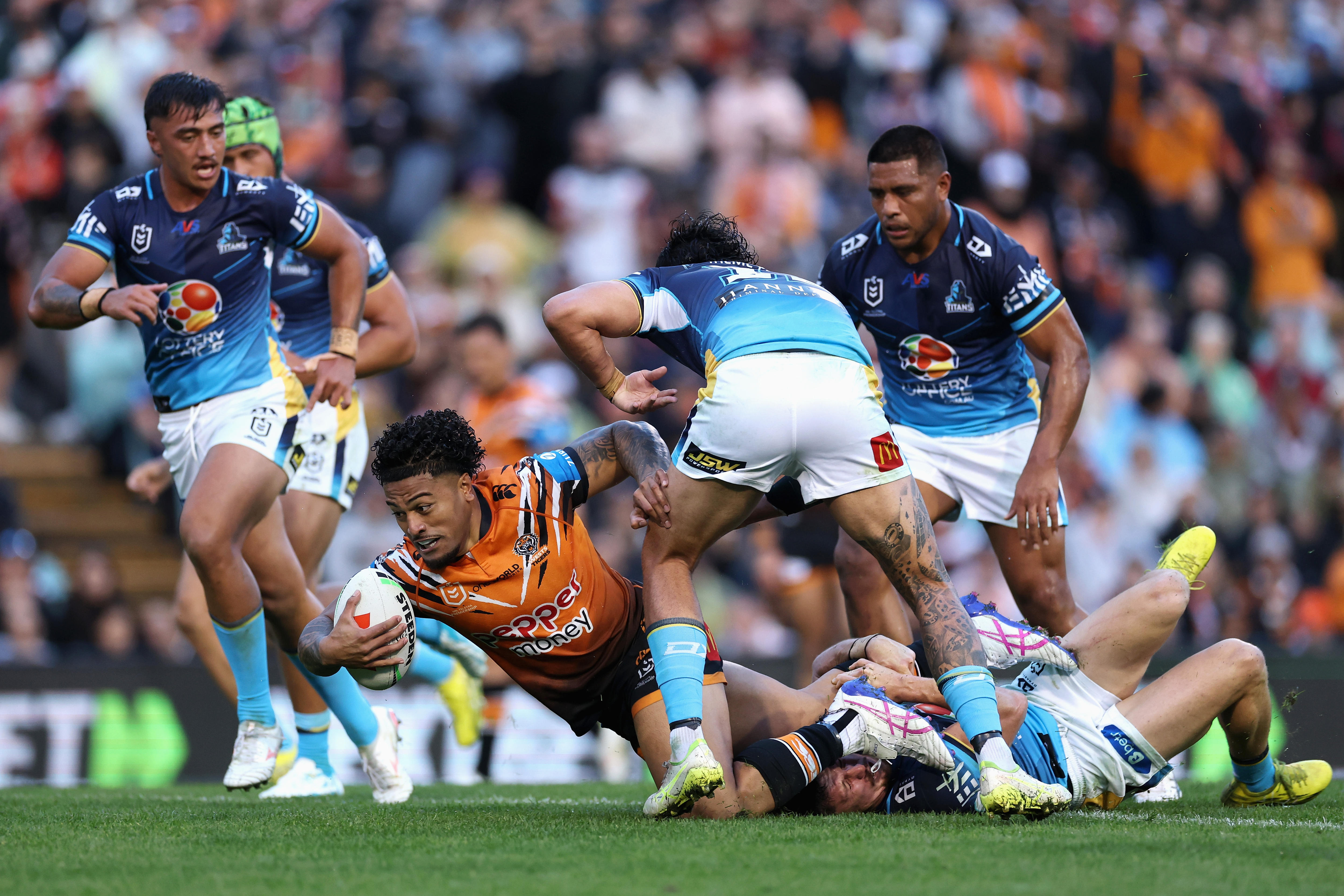 A rugby league player in orange dives with the ball being tackled by players in blue