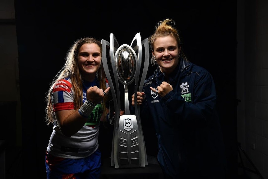 Two women standing on either side of large sports trophy.