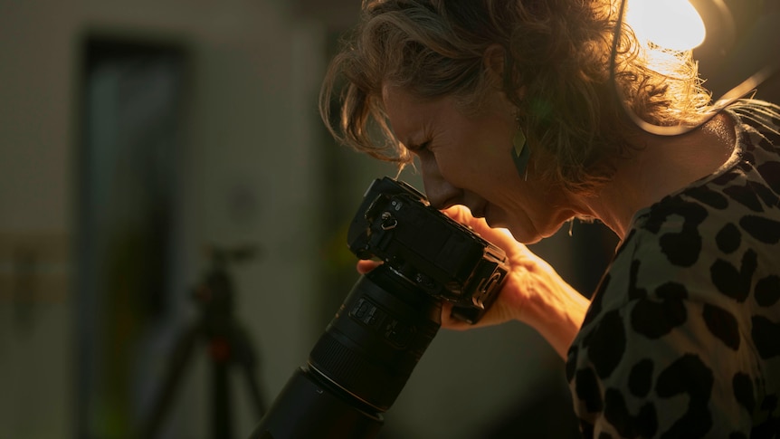 A woman looks through a camera lens.