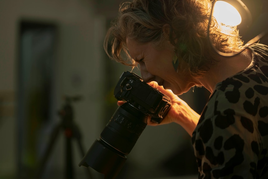 A woman looks through a camera lens.