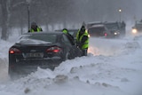 People try to push a car that became stuck in heavy snow during a blizzard at night in Dublin.