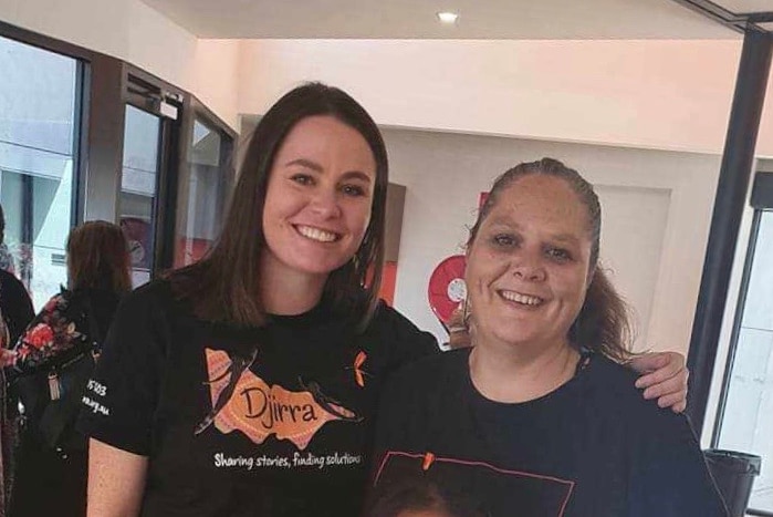 Two women smile in an embrace and smile at the camera