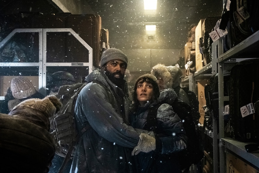 Two people embrace as they enter a train carriage with snow around them