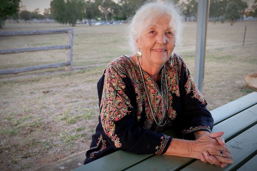 A woman smiling, sitting outdoors, leaning on a picnic table