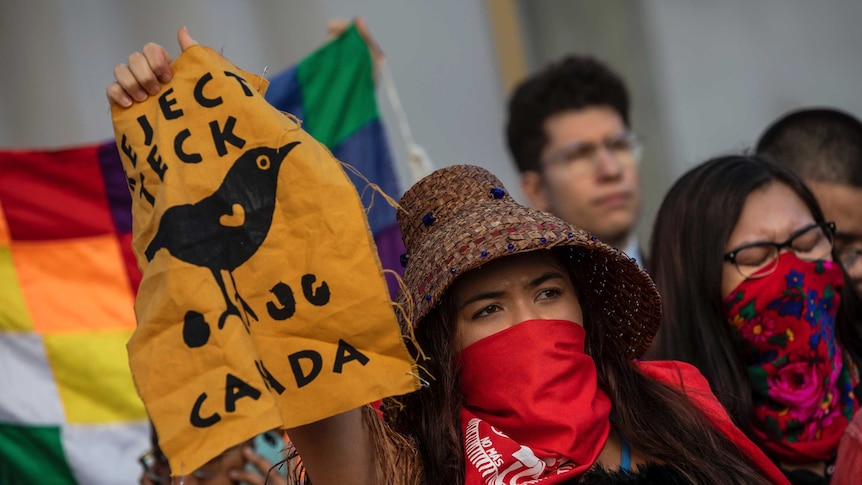 A woman holds up a sign with a picture of a bird in a crowd of protesters.