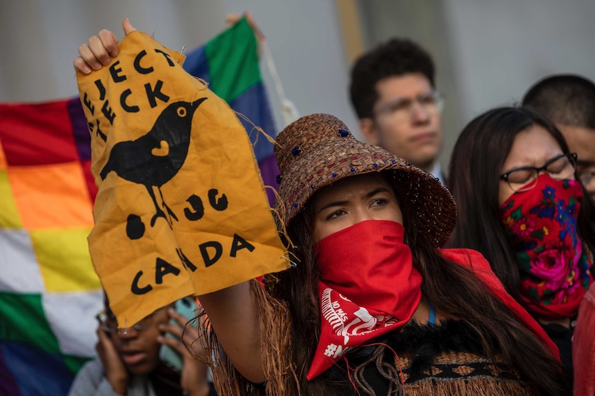 A woman holds up a sign with a picture of a bird in a crowd of protesters.