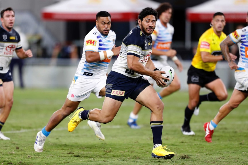 A North Queensland Cowboys NRL player runs with the ball as the opposition team chases him.