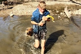 Stuart Moodie holding a carp he's caught in a waterhole in the Mole River