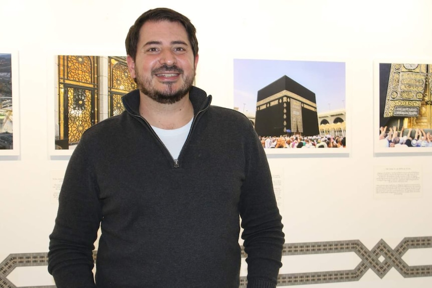 Photographer Mark Zed with his exhibition work on the wall behind him.