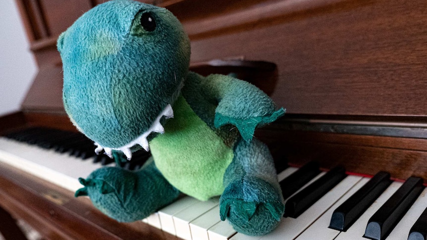 A plush toy dinosaur sitting on a piano