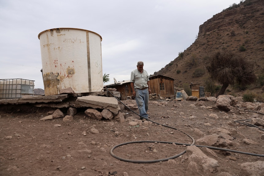 A rancher stands next to a water tank used for his animals. 