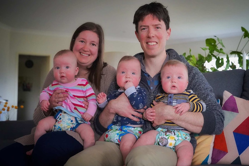 A couple sit on a couch with their three young children.