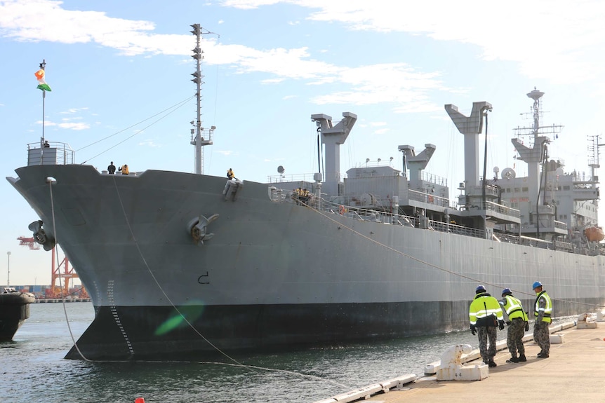 INS Jyoti comes into dock at Fremantle Harbour, as workers in hi vis gear prepare.