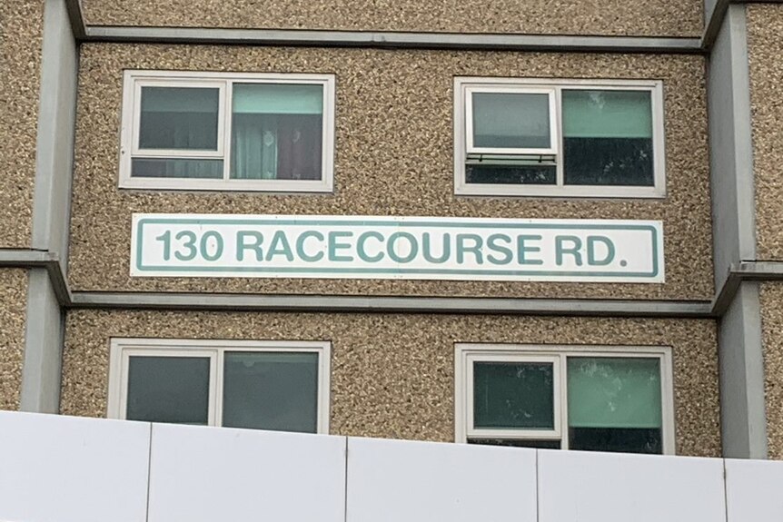 A sign reads '130 Racecourse Road' on the side of a high-rise public housing tower.