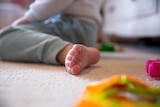 A close-up of a child's toes who's sitting on the floor.