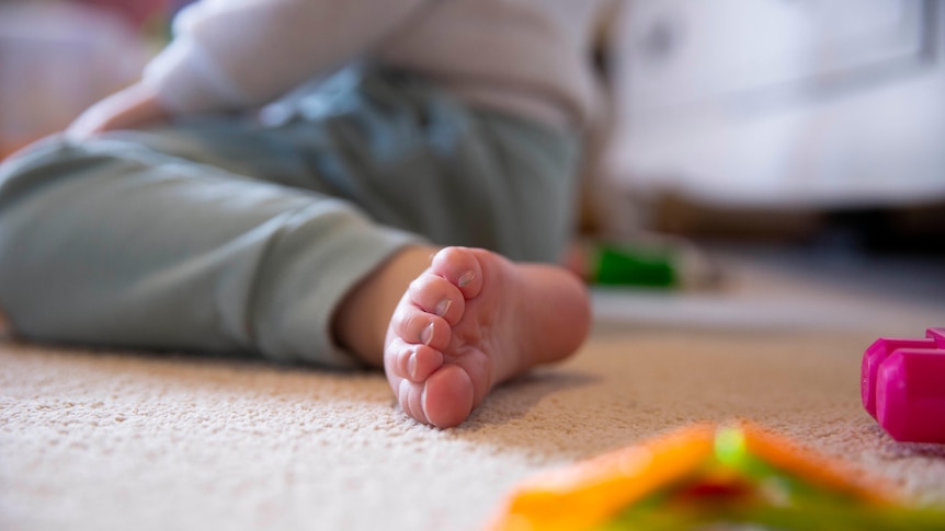 A close-up of a child's toes who's sitting on the floor.