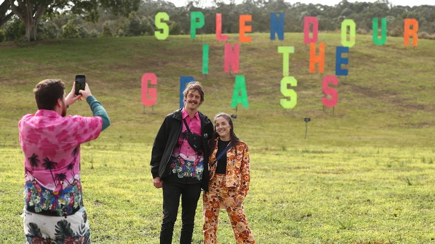 Two people stand in a field with large letters sitting on a hill behind them