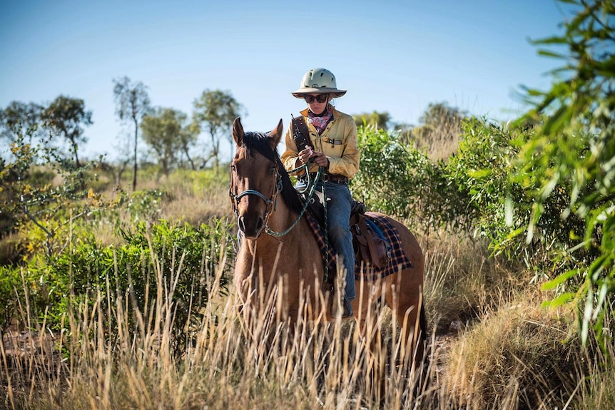 A woman on a horse wearing a helmet in the outback