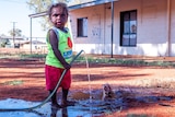 An Aboriginal child about 5-years-old holds a leaky hose