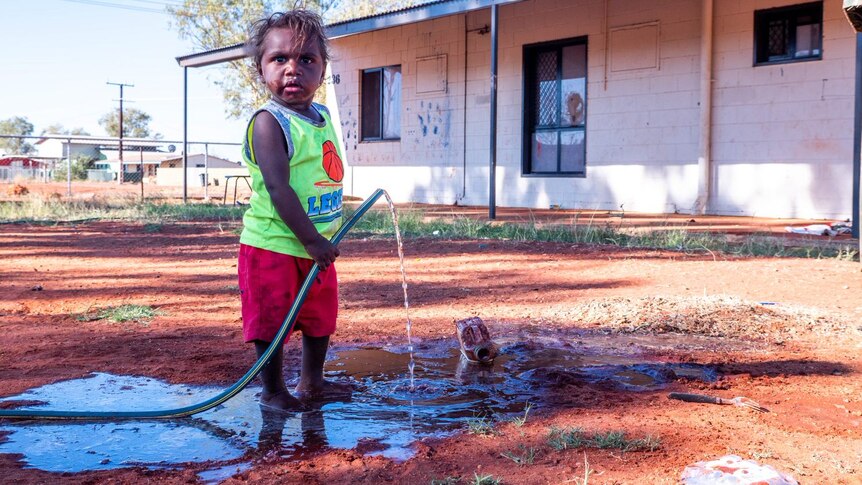 An Aboriginal child about 5 years old holds a leaky hose