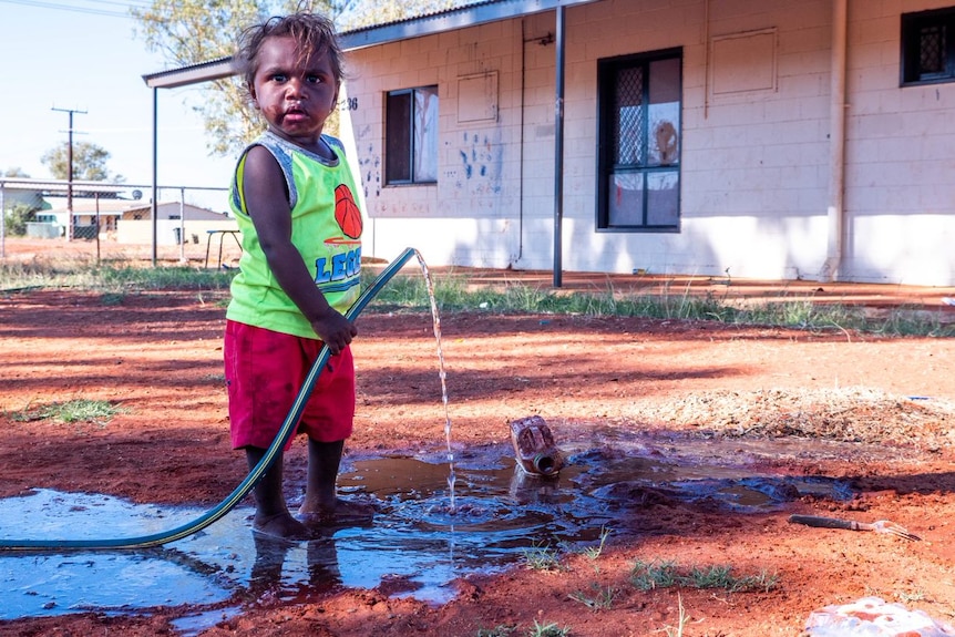 An Aboriginal child about 5-years-old holds a leaky hose