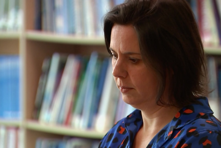 Woman with white skin, short brown hair and bright blue shirt in front of library shelf