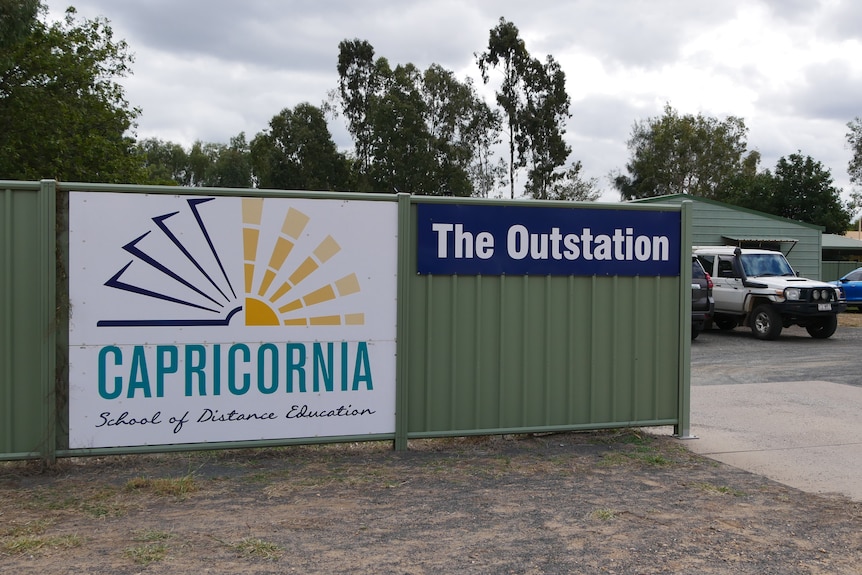 A steel fence with a sign of the school and the camping spot "The Outstation"