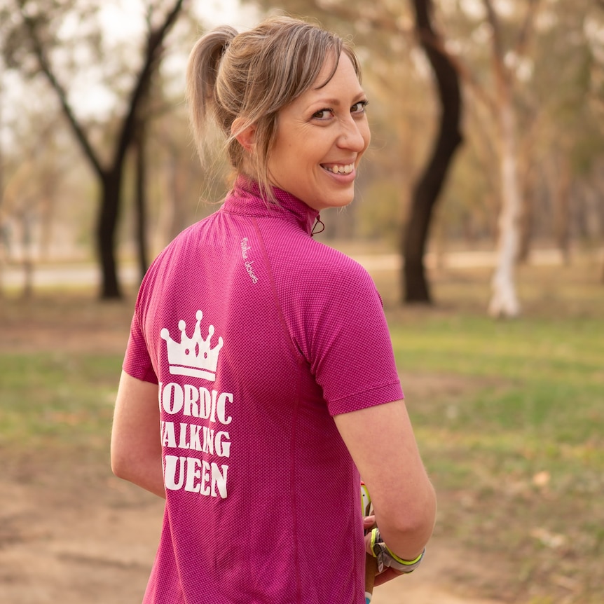 A woman on a walking track, wearing a t-shirt that says "Nordic walking queen".