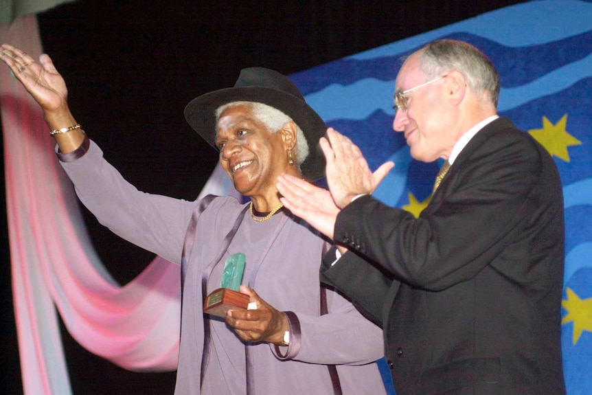 Evelyn Scott holds a trophy and raises her hand while former PM John Howard applauds.