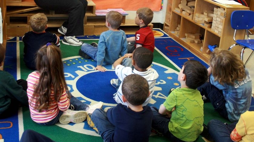 Young children sit on the floor of a classroom