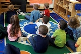 Young children sit on the floor of a classroom