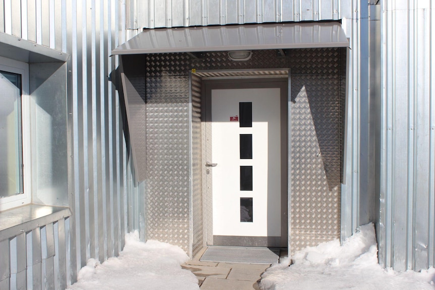 A solid metal door with ice, snow and grey stone around it