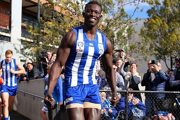 Majak Daw smiles as he runs on to a football ground while fans behind him take photos.