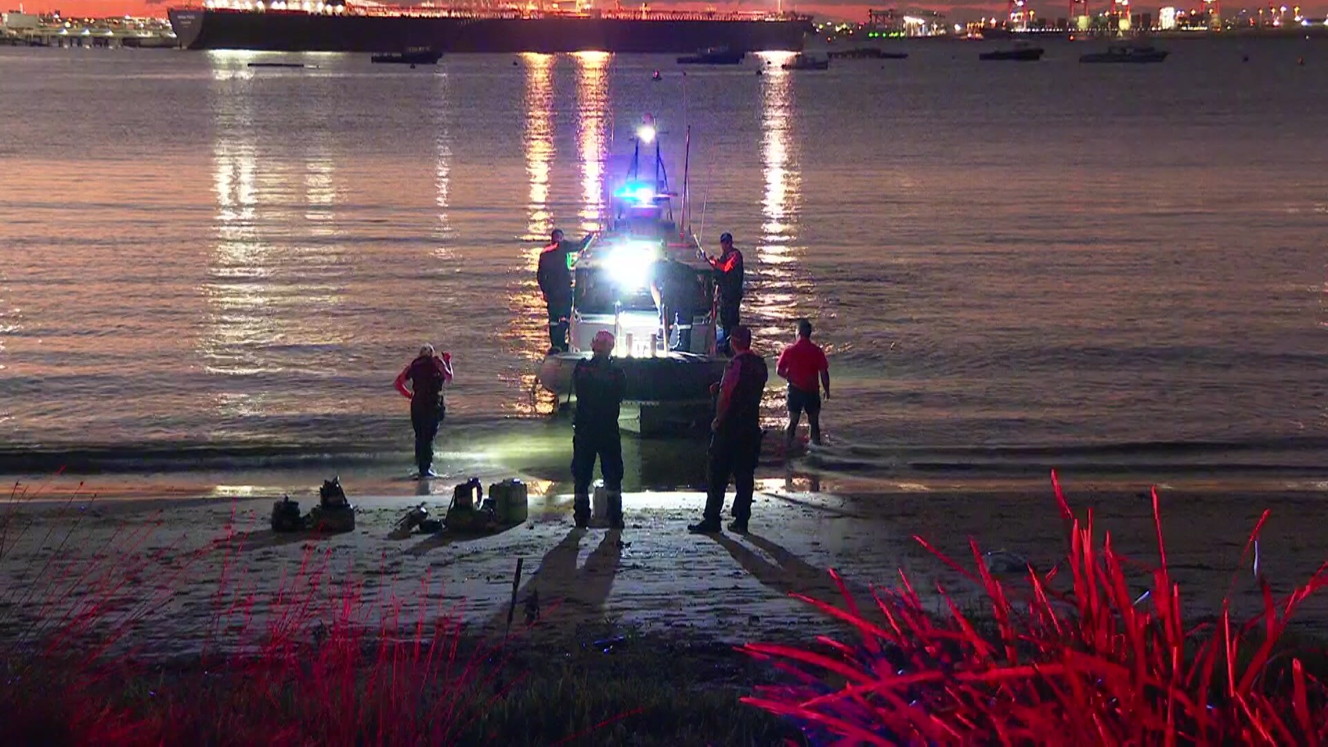 A boat by the shore with people surrounding it in the late afternoon.
