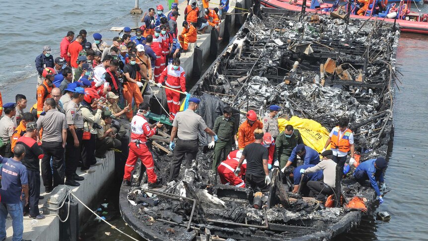 People on and near the burnt remains of the ferry, ferry still on the water.