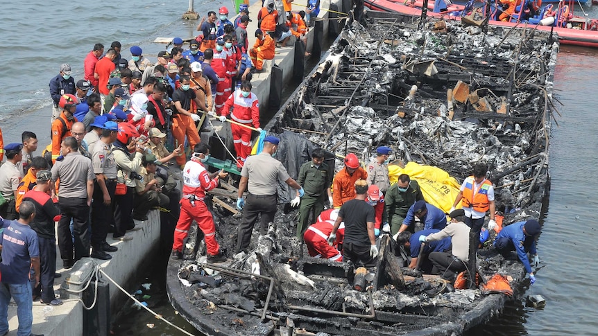 People on and near the burnt remains of the ferry, ferry still on the water.