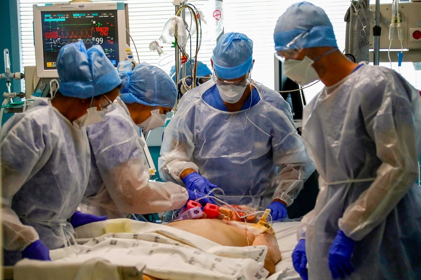 A group of health workers in PPE surround a male patient on a stretcher