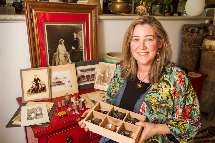 Woman sitting in front of old photographs holding a box of Chinese artefacts.