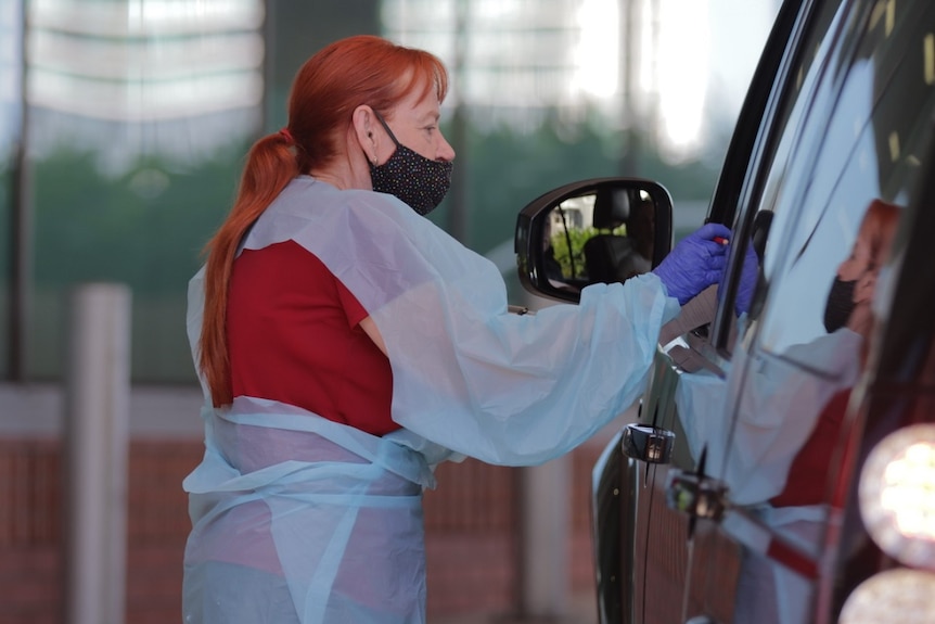 Woman in personal protective gear swabs a patient through a car window
