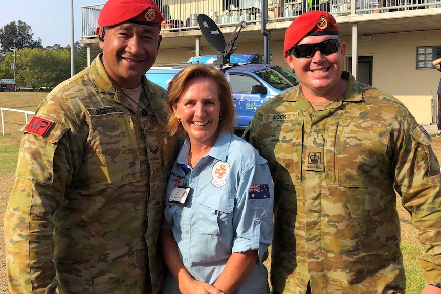 A woman wearing a blue shirt stands between two men in Army Military Police uniforms