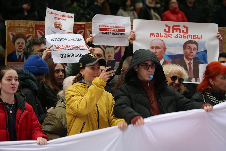 A group of people hold banners and placards, one featuring Putin next to Georgian former Prime Minister Bidzina Ivanishvili