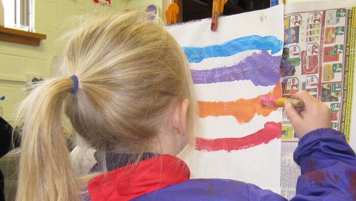 Unidentifiable five year old girl painting at a easel at a child care centre.
