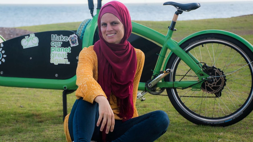 A lady sitting in front of her bike by the waterfront.