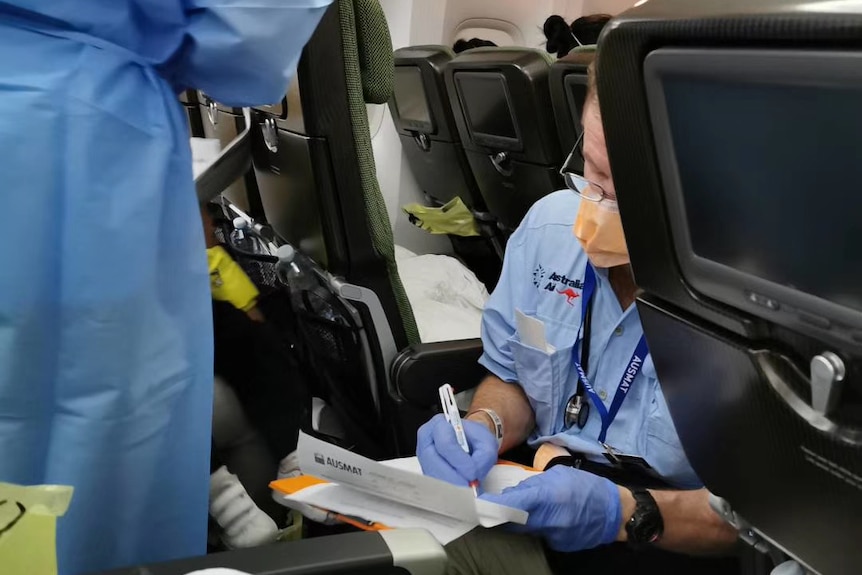 A doctor with a face mask writes on a piece of paper inside a plane.