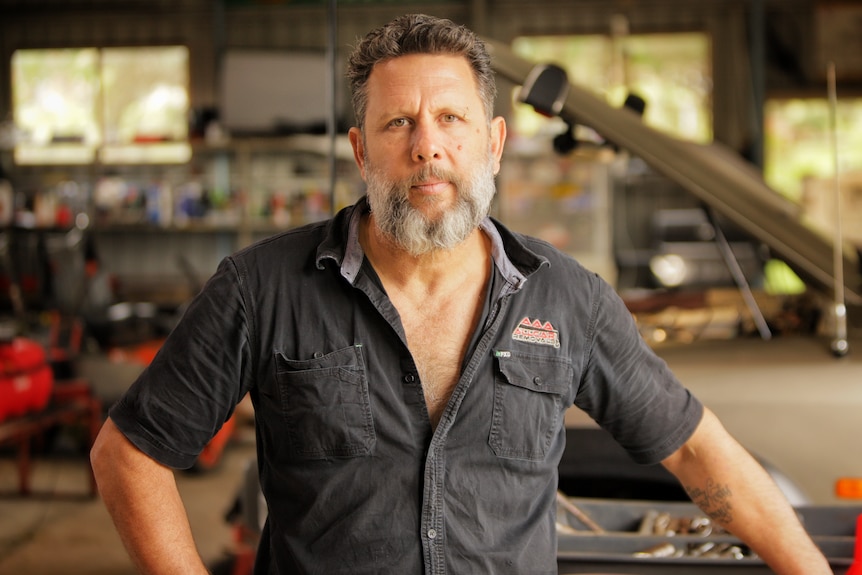 Man standing in a workshop wearing a black shirt.