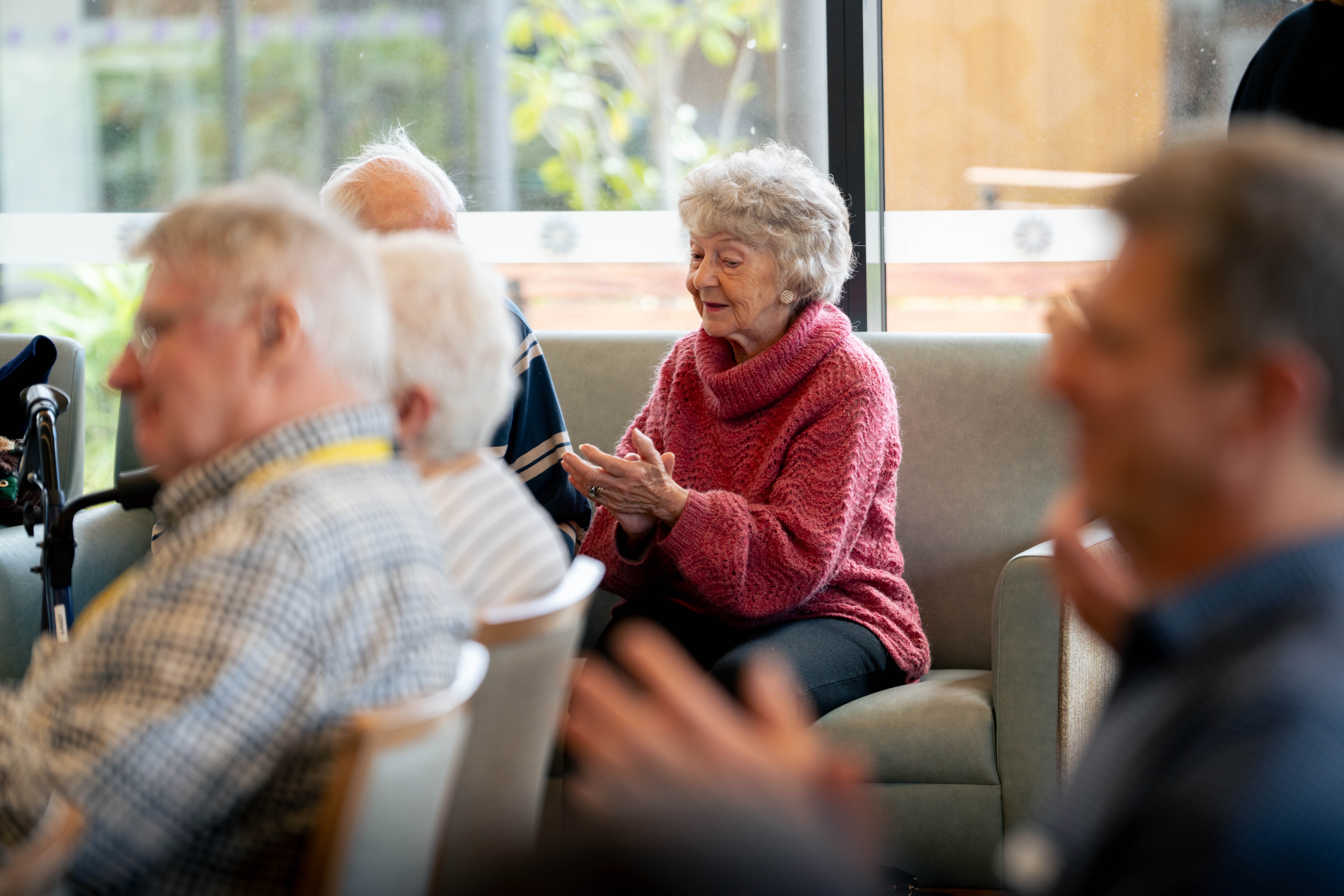 Mature-aged people sit in rows of chairs looking ahead, listening to music.