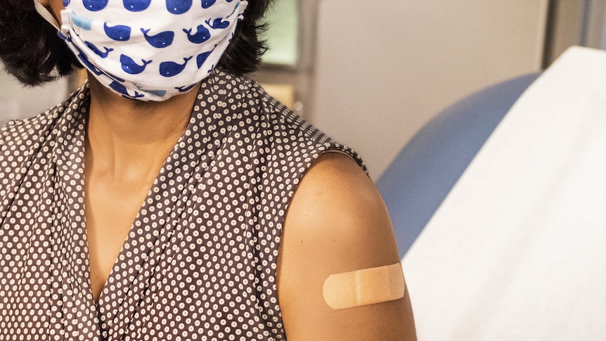 A patient wearing a mask with a band-aid on their upper arm like they've just been vaccinated. 
